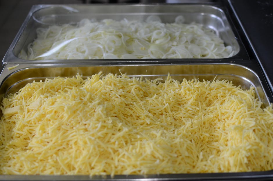 Close-up of shredded cheese and sliced onions in metal trays, perfect for cooking or catering setups