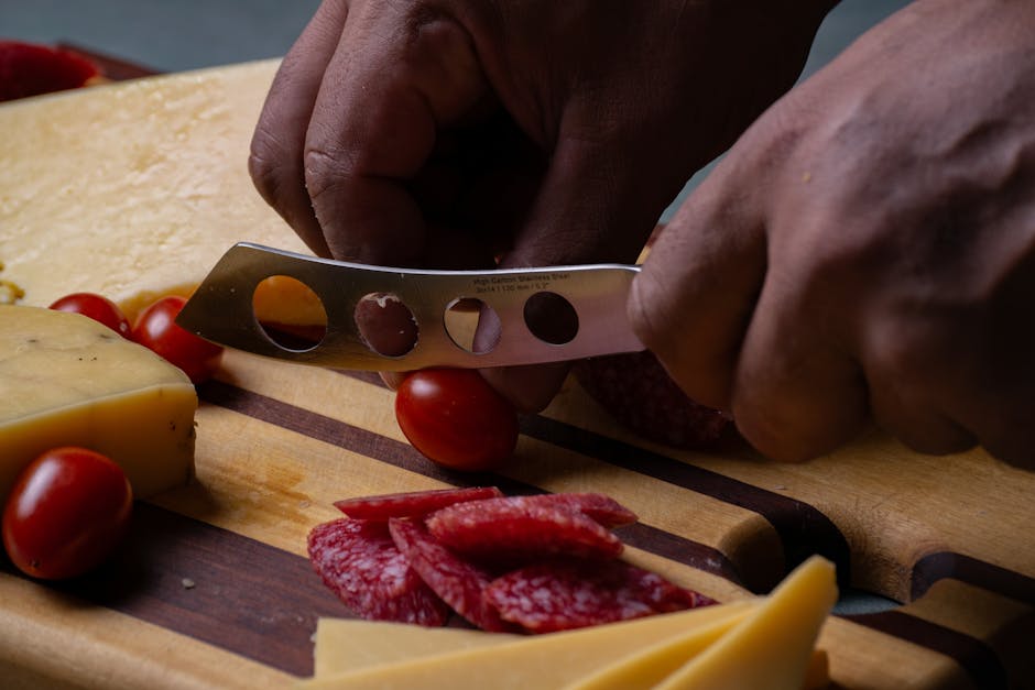 Close-up of hands slicing salami on a meat and cheese platter with knife and cherry tomatoes
