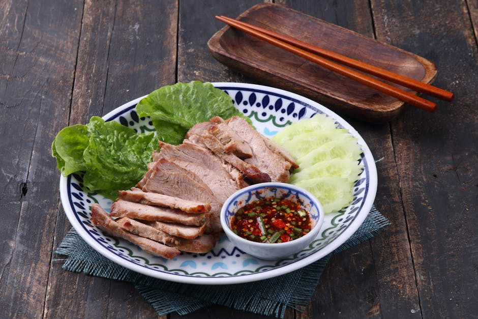 Grilled pork slices with spicy dipping sauce, cucumbers, and lettuce on a decorative plate