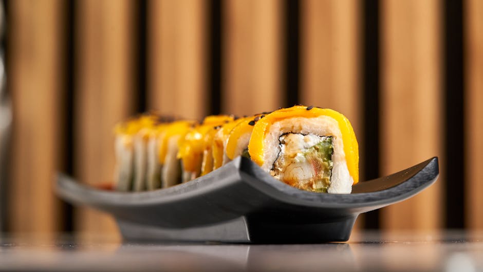 Gourmet sushi roll topped with fresh mango slices, beautifully presented on a ceramic plate